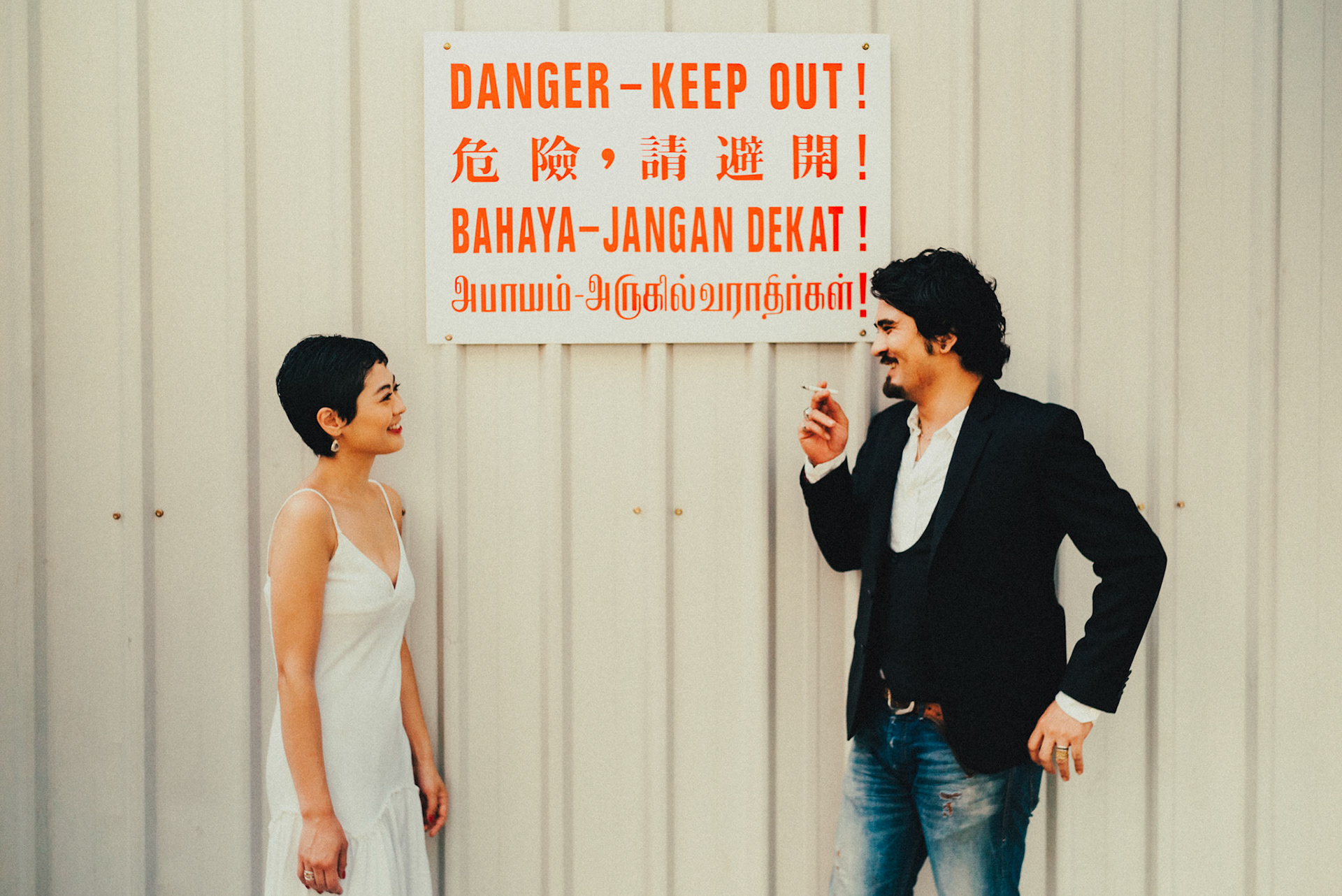 A Japanese couple sharing a moment in front of a mundane construction warning sign, cigarette on hand, from Ibuki and Emi's casual chill engagement shoot, Little India, Singapore, October 2015, Sony A7S.