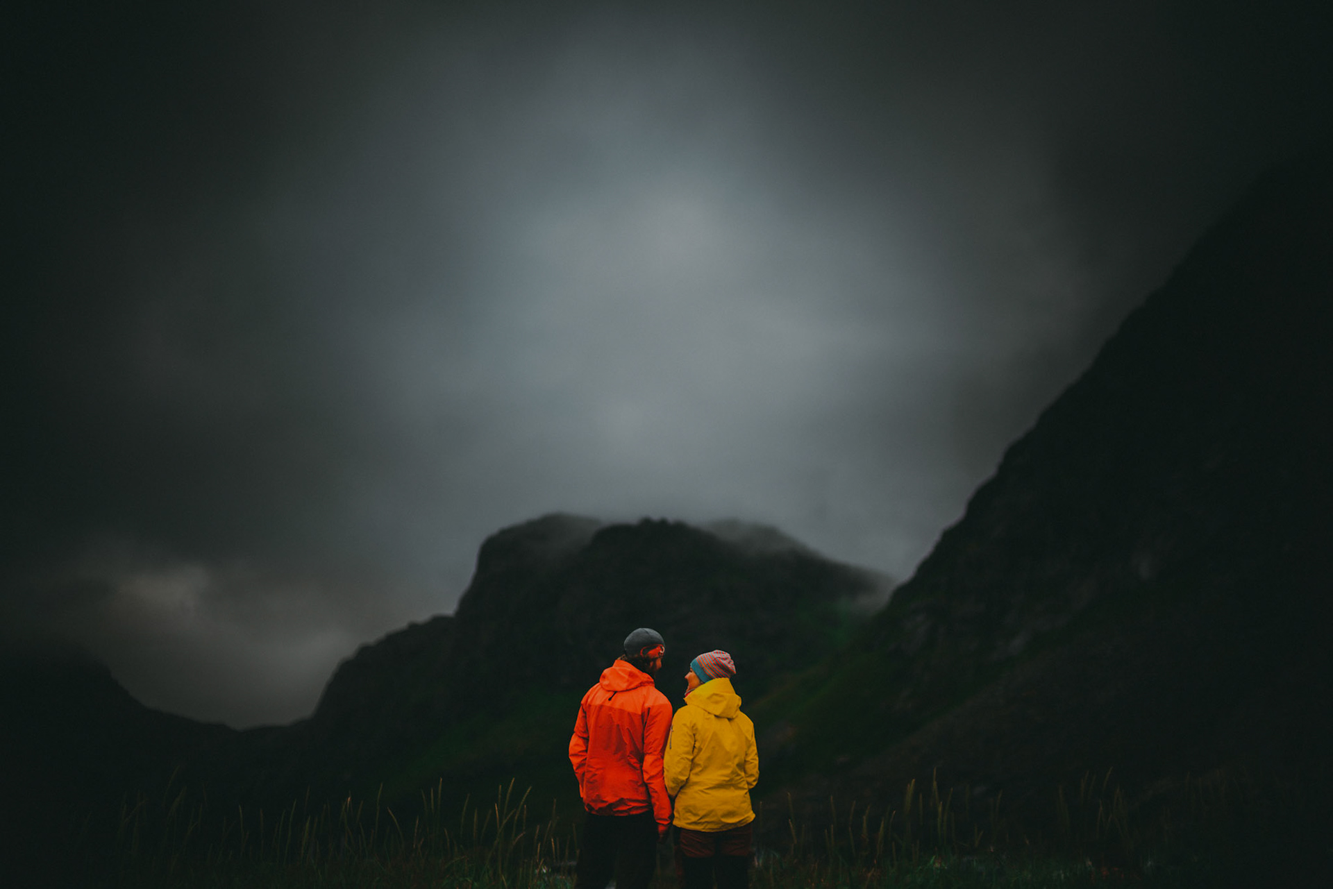 A couple wearing outdoor hiking apparel in front of foggy hilltops, Lofoten Islands, Norway, July 2016, Sony A7RII.