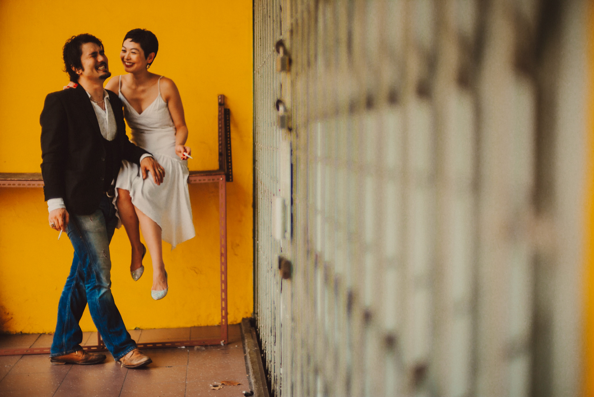 A Japanese couple in front of a bright yellow wall, from Ibuki and Emi's casual chill engagement shoot, Little India, Singapore, October 2015, Sony A7S.
