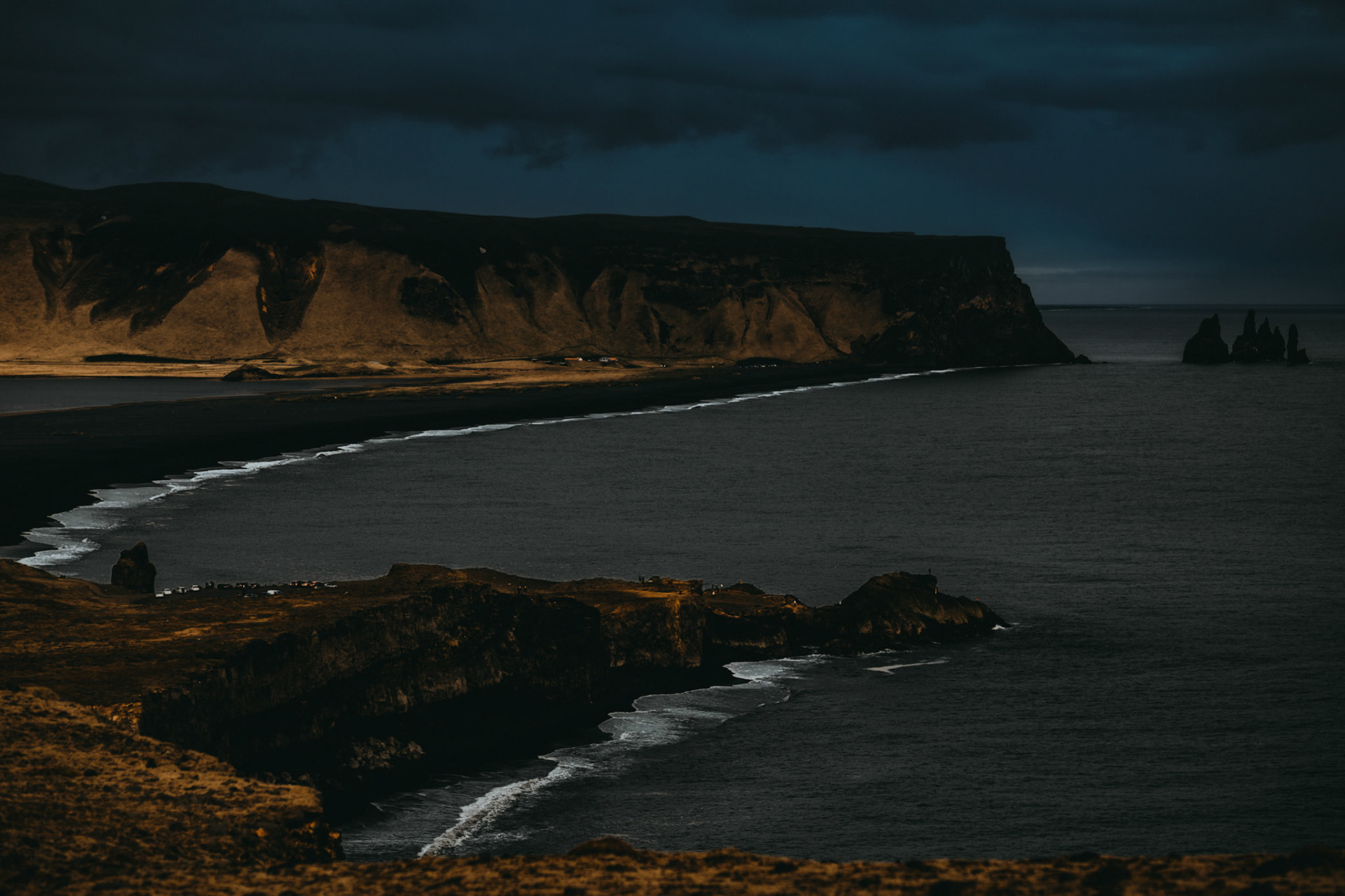 A long stretch of black sand beach and a plateau against a moody sky, as seen from Dyrhólaey Viewpoint, Iceland, May 2016, Sony A7RII.