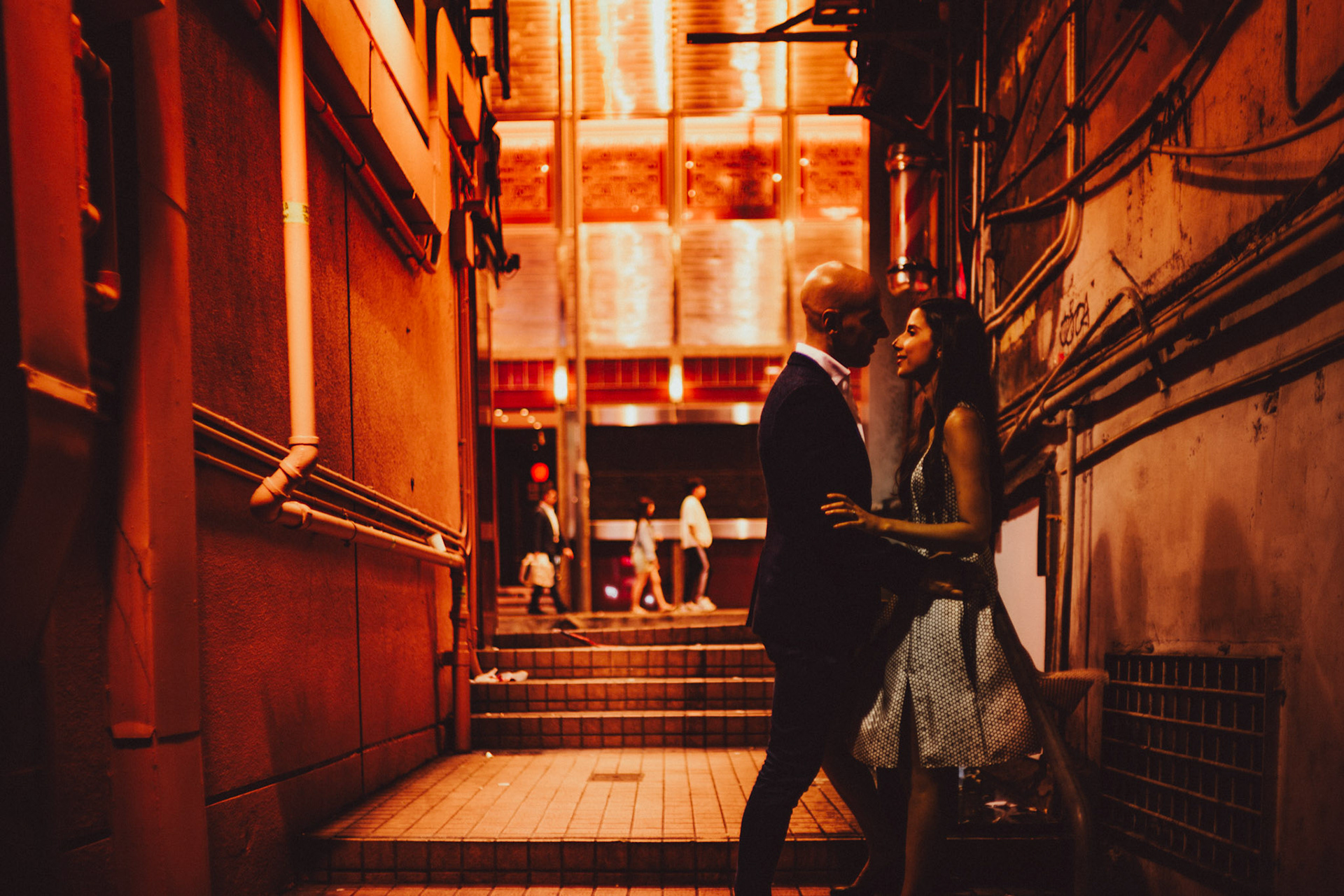 A moody and intimate late night urban engagement shoot in one of Stanley Street's alleyways with passers-by in the background, from Eric and Sabrina's prewedding shoot in Central, Hong Kong, April 2019, Sony A7III.