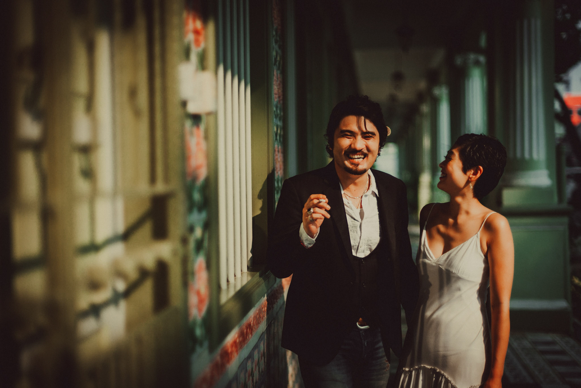 A Japanese couple sharing a lighthearted moment in a sunlit corridor with Peranakan details, from Ibuki and Emi's candid chill engagement shoot, Pertain Road, Little India, Singapore, October 2015, Leica M.