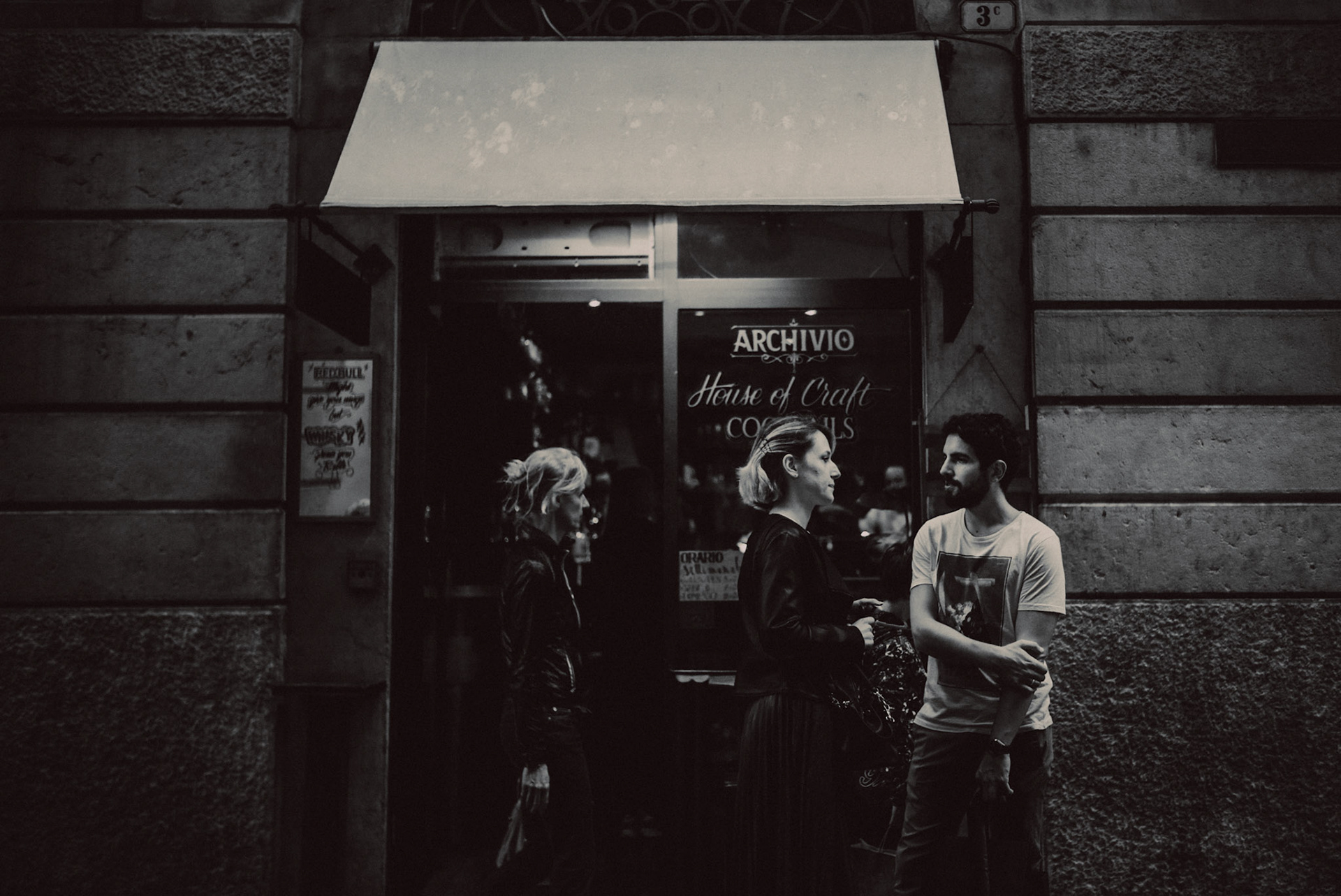 Pedestrians walking in front of Archivio Bar, in black and white, Verona, Italy, September 2017, Leica M.
