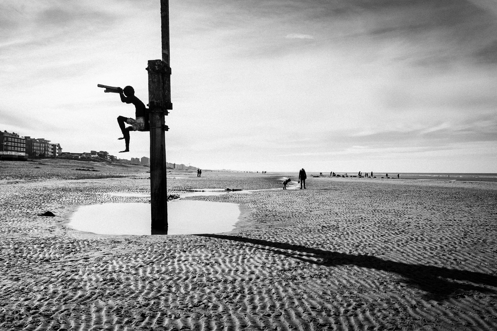 Kunst op strandpalen. Een gesmaakt initiatief met de naam Getij-Dingen. Bij vloed komen de palen al dan niet gedeeltelijk onder water te staan, zo ook het kunstwerk dat erop gemonteerd is. En dat ondergaat dus evenzeer de kracht van de zee en de medogenloze inwerking van het zeezout. Dit mannetje heeft geen oog voor de zee. Hij tuurt naar de appartementen op de dijk. Misschien wel als ultieme wraak op de stiekemerds die vanop hun terras naar de twee meisjes met modebladen op het strand gluren.
