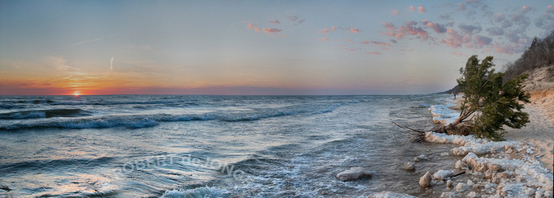 A late Winter panorama of the sun setting on Lake Michigan — the Lake tree clinging to an ice ledge on shore.