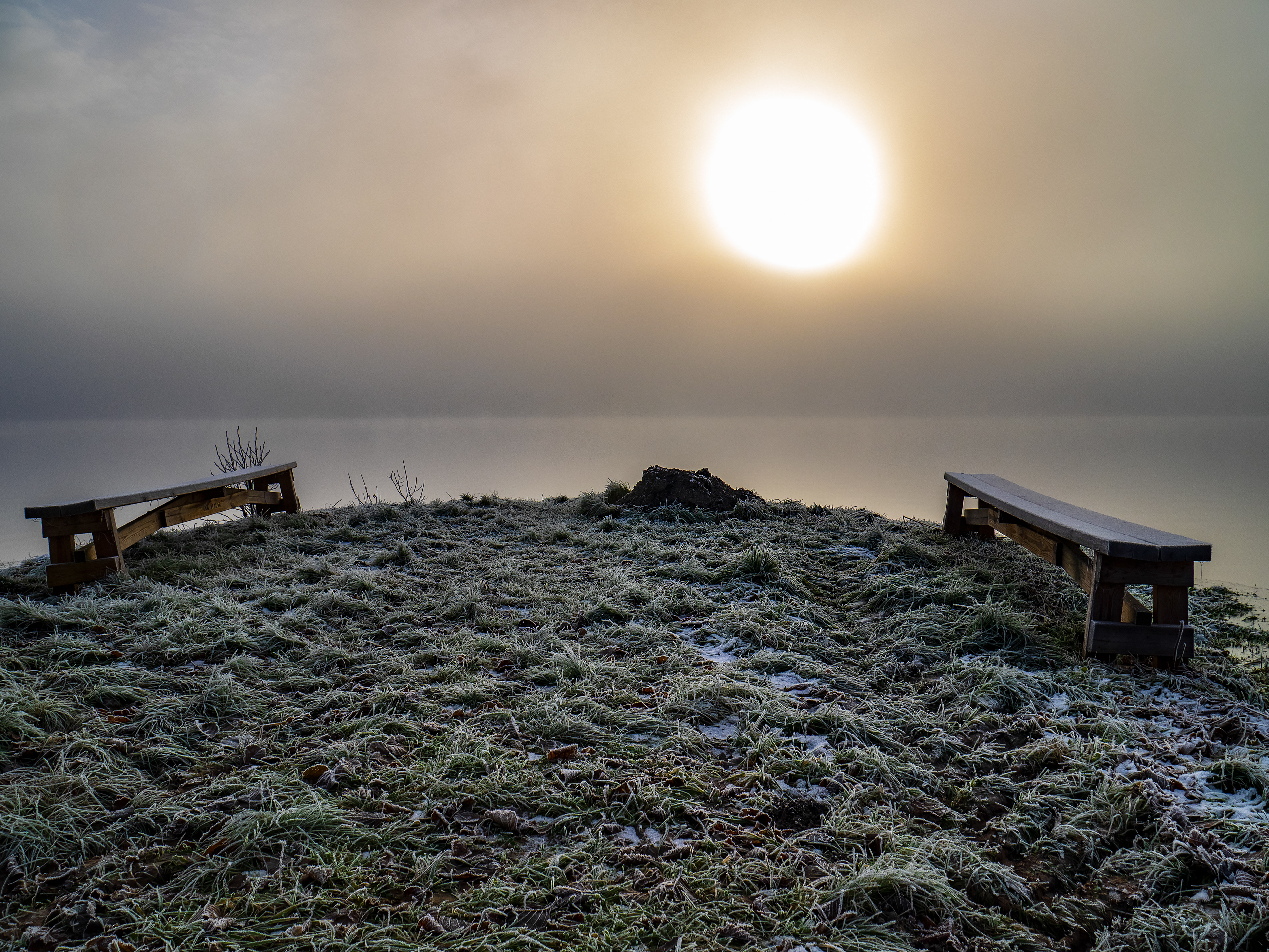 2 benches on the edge of a frozen lake on a hazy winter morning in Sweden. 