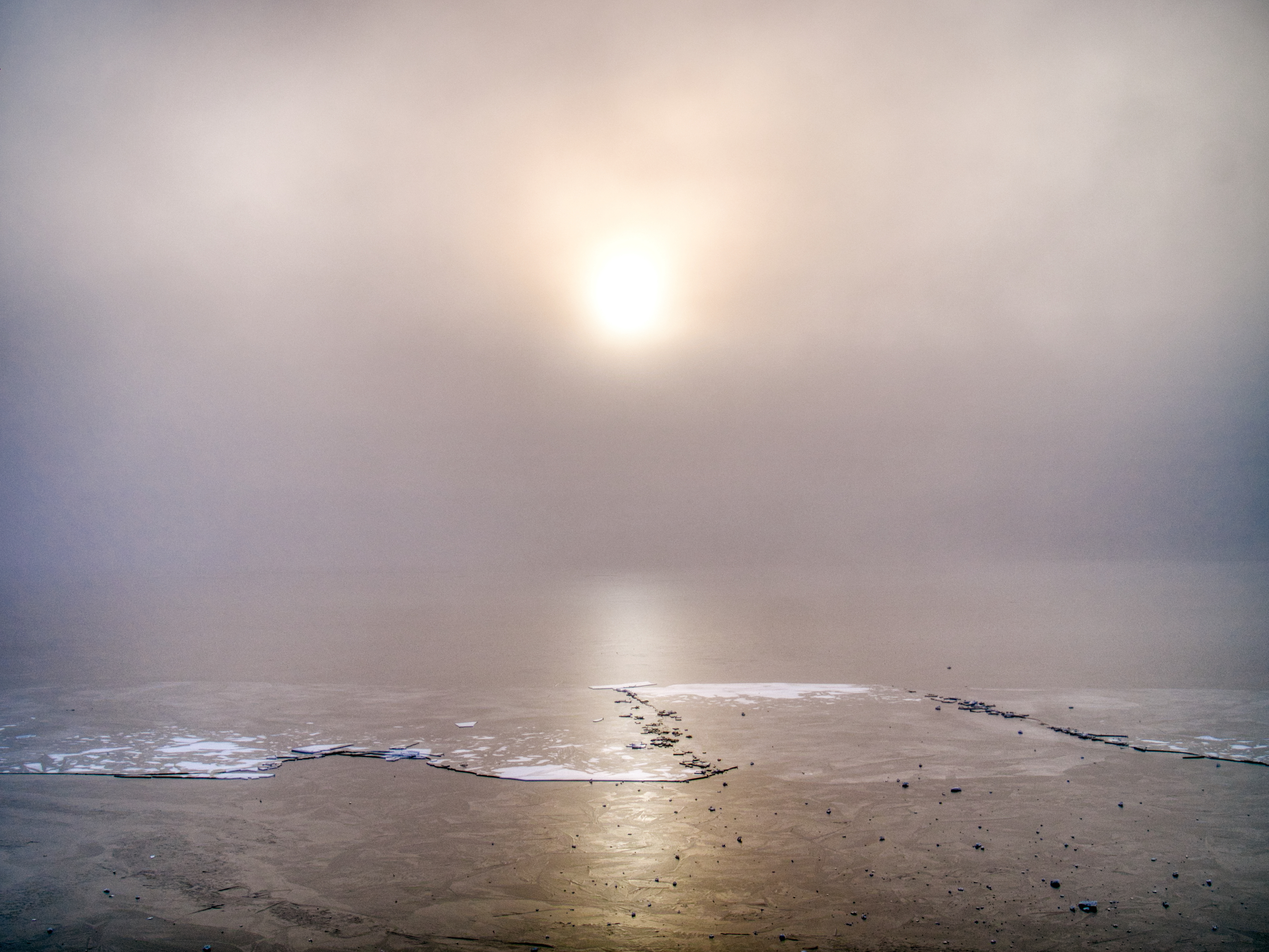 Frozen lake,icy surface and haze with the sun trying to break through. Minimalistic with only  lines on the ice 