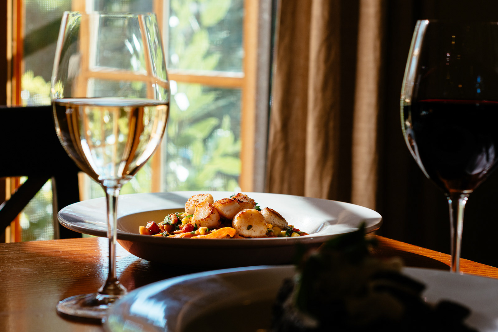 Dinner plate with glass of wine on table near a sunny window at Grit Kitchen in Eugene