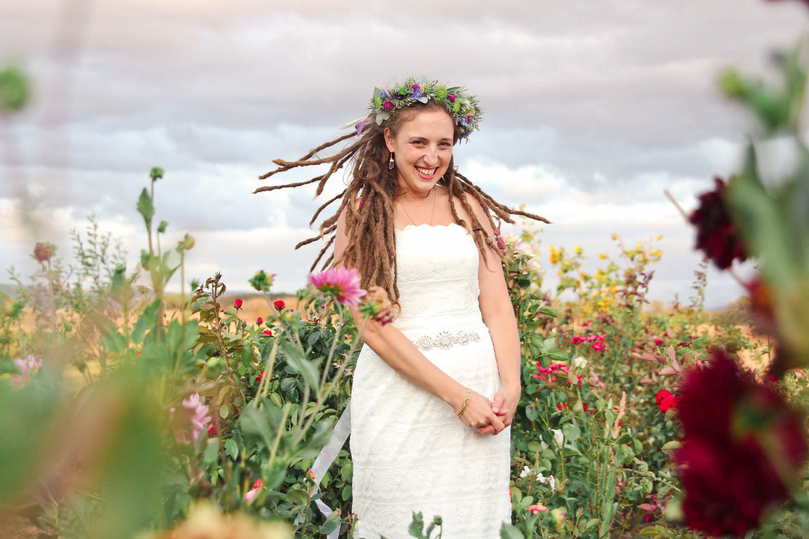 Bride in white dress and flower crown smiling in a field of wildflowers