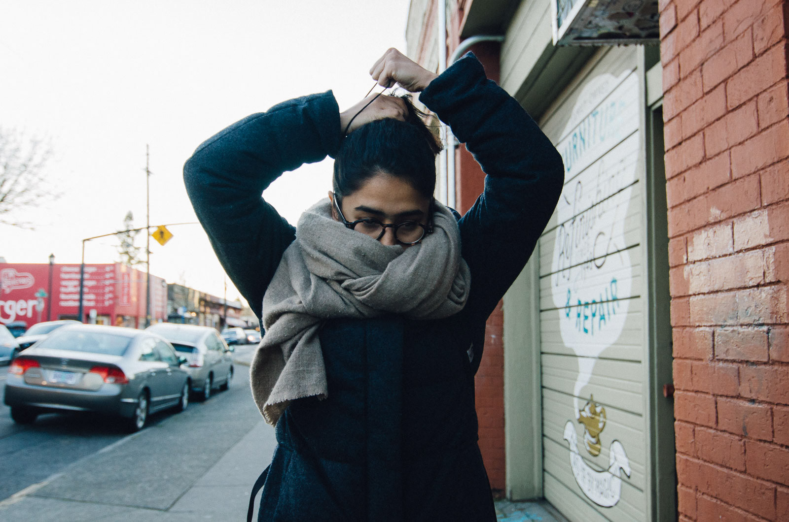 Street scene of woman tying up her hair, wrapped in a thick scarf