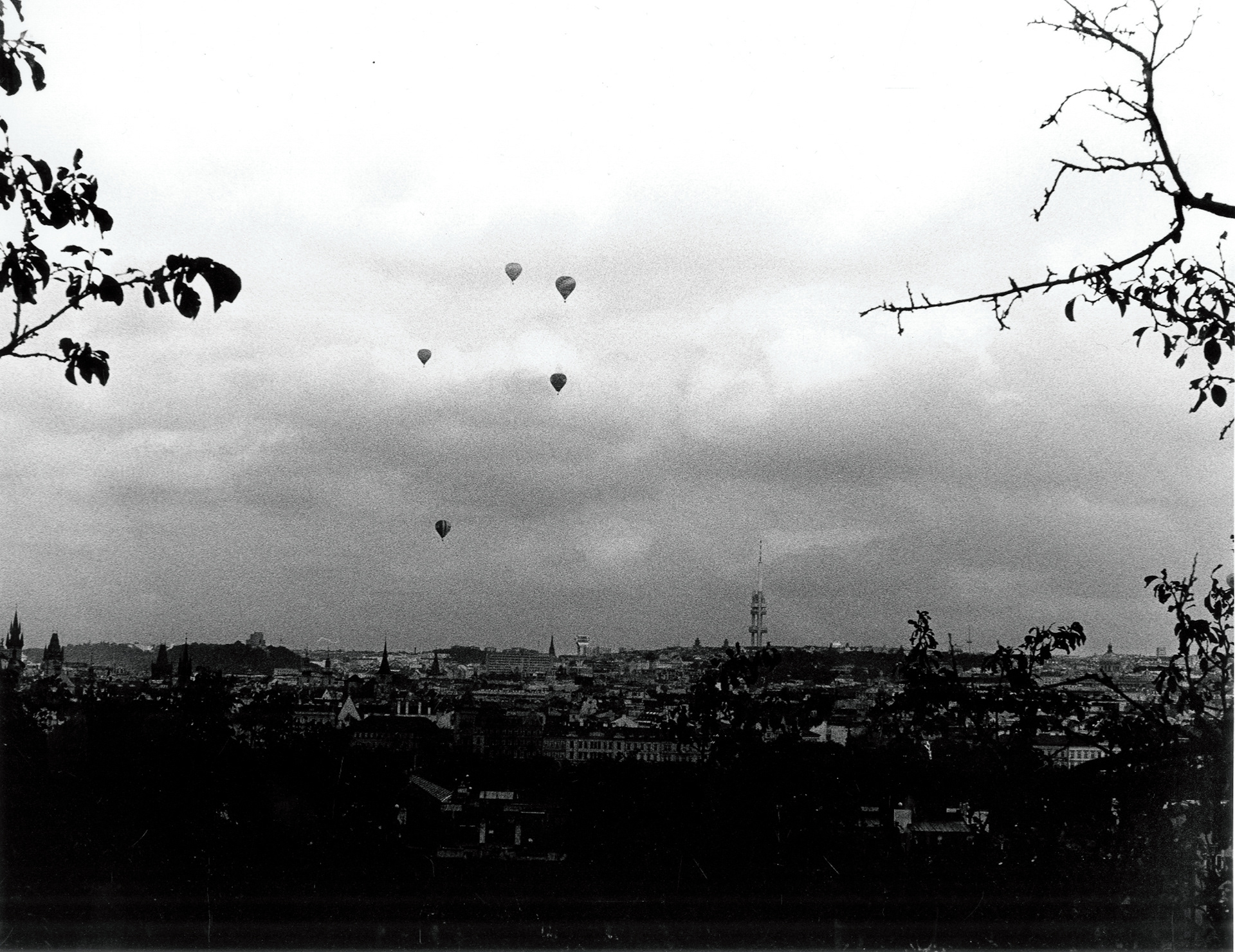 a cityscape of Prague taken from above, in the sky are 5 hot air balloons