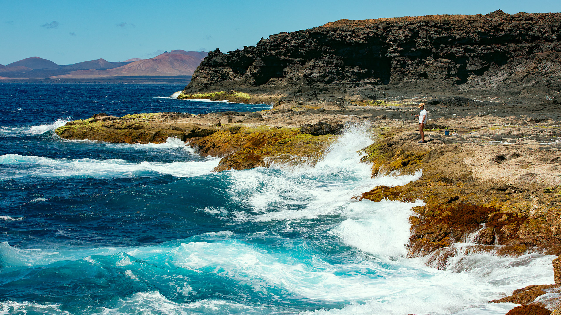Fischer in der Brandung der Atlantikküste im Hintergrund rote Vulkane, fotobagaluten, Lanzarote, Kanarische Inseln