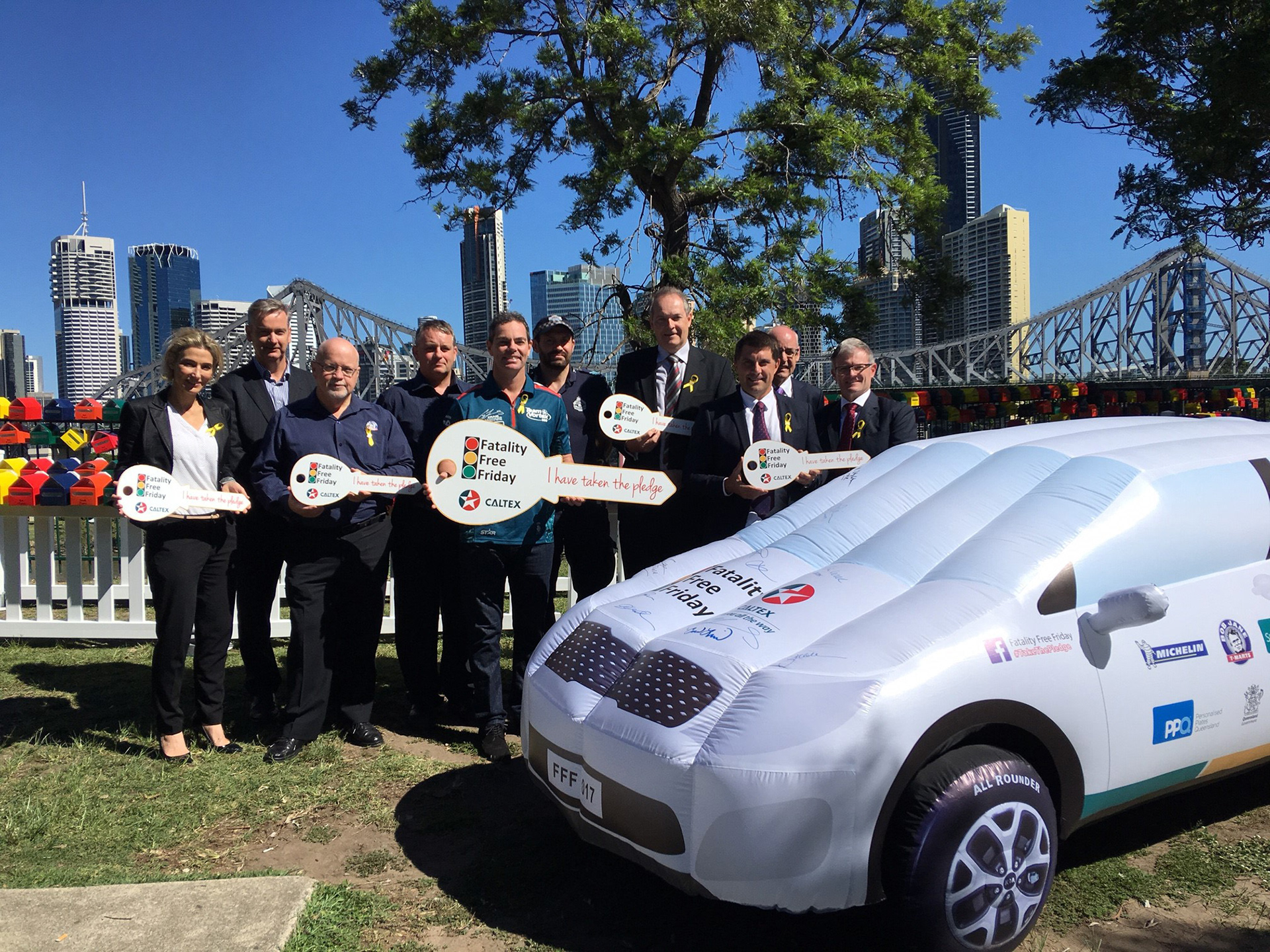 Group photograph around blow-up Fatality Free Friday Car which is covered in signatures.