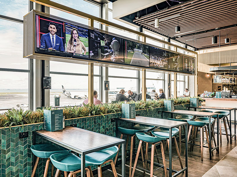 Beautiful green chevron Skeme tiles have been used as cladding to low height walls,, with brass framing to bring the high ceiling down at seating areas.