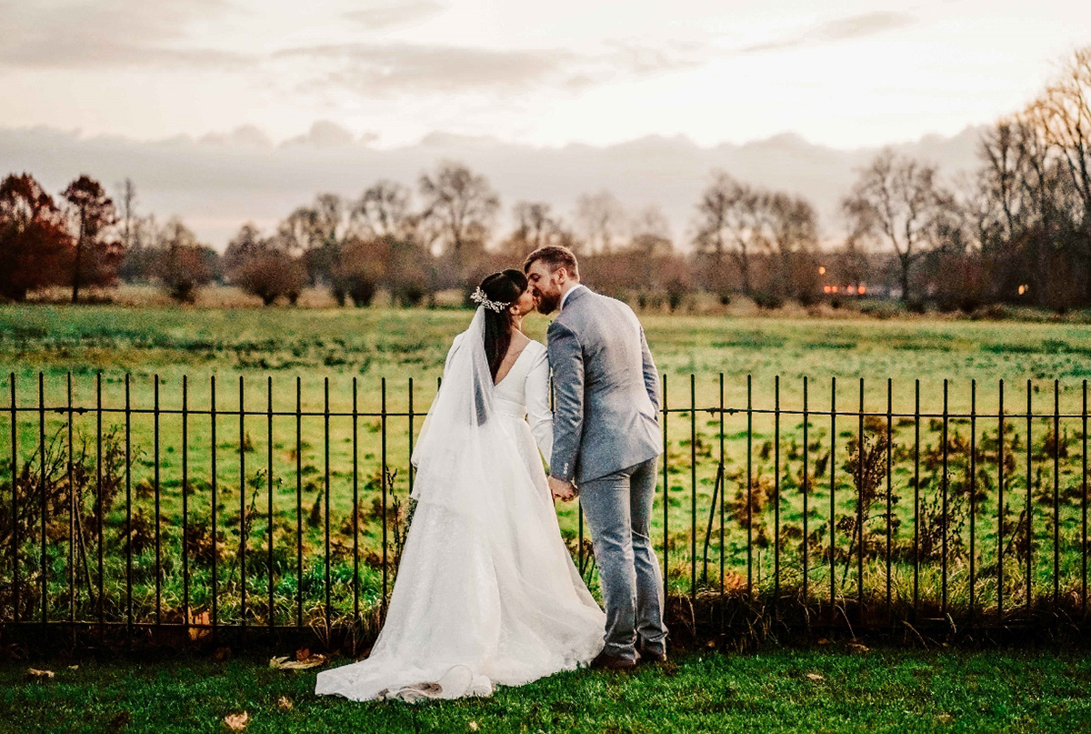 bride and groom kissing in candid photo by david lefebvre stood by oxfordshire field near town hall after covid wedding in december during golden hour