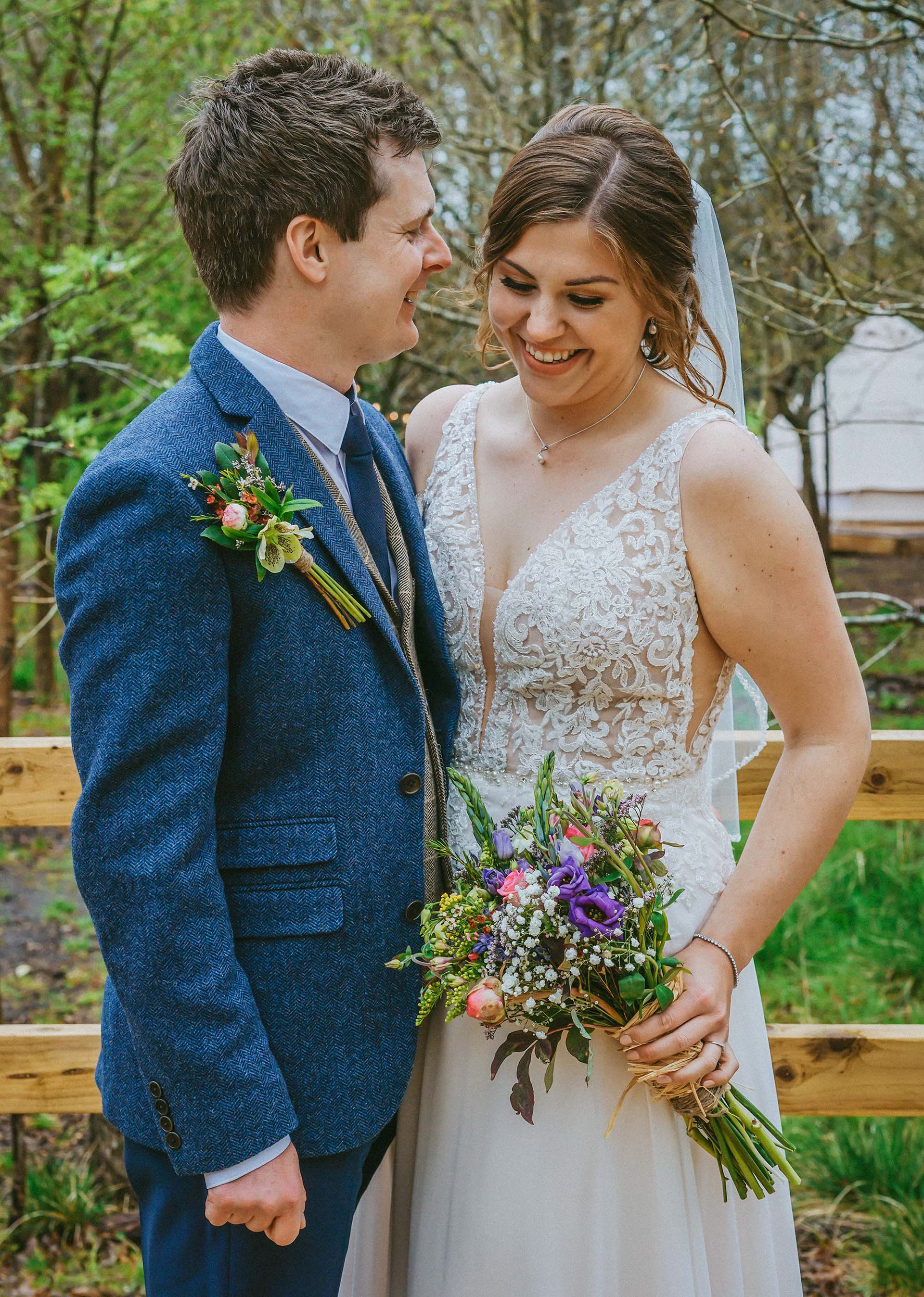 loving candid moment after wedding ceremony down in buckinghamshire woods with bride and groom smiling together and holding each other looking with fresh flower bouquet