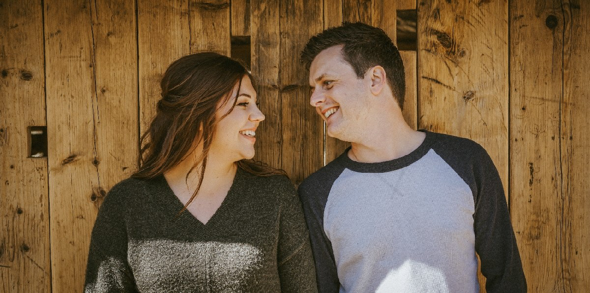 smiling engaged couple leant on wooden wall in stunning wedding venue called endeavour weddings in swanbourne the couple are on an engagement shoot with photographer david lefebvre