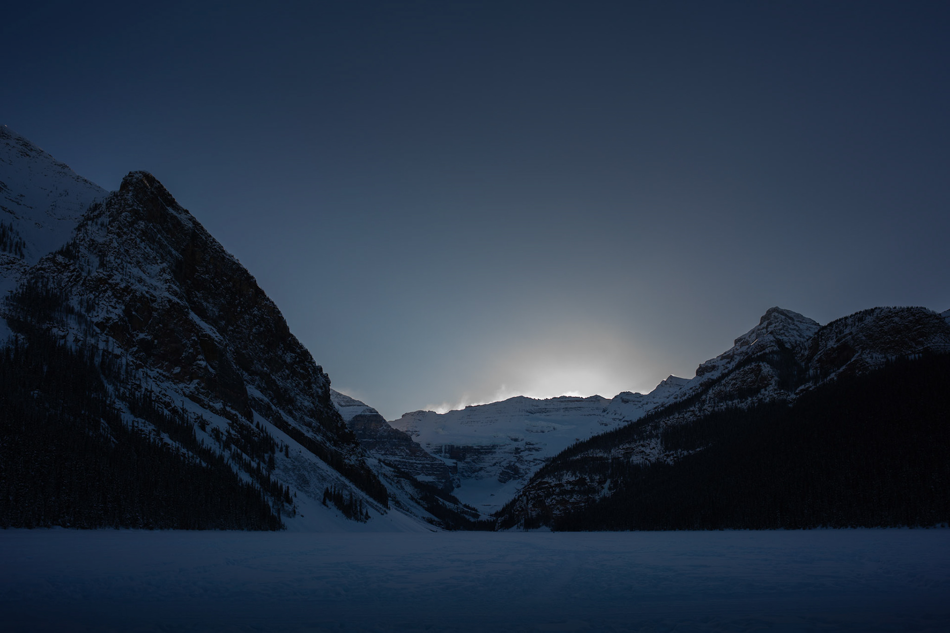 Sun setting behind the mountains at Lake Louise spotlights the blowing snow along the mountain tops