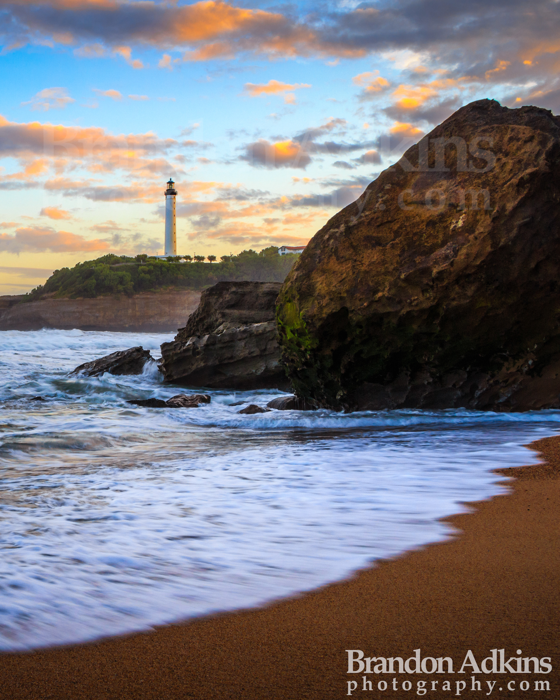 Fine art photograph of light house and boulders in foreground with colorful sky at sunrise in Biarritz, Basque region of France