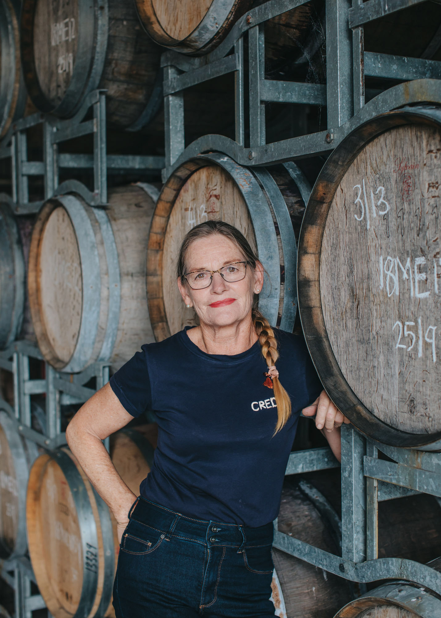 Winemaker Jenny Dobson posing in front of wine barrels for magazine photoshoot.