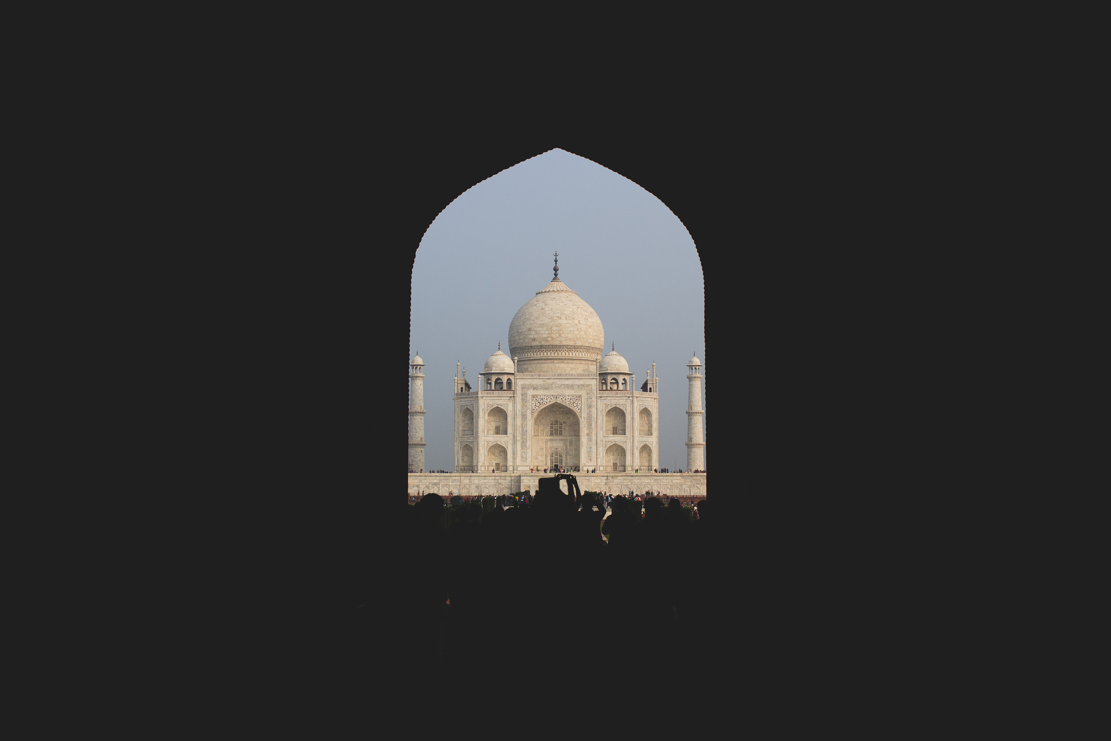 Image shows the Taj Mahal, a beautiful symmetrical marble building framed by black, created by the entrance gate building