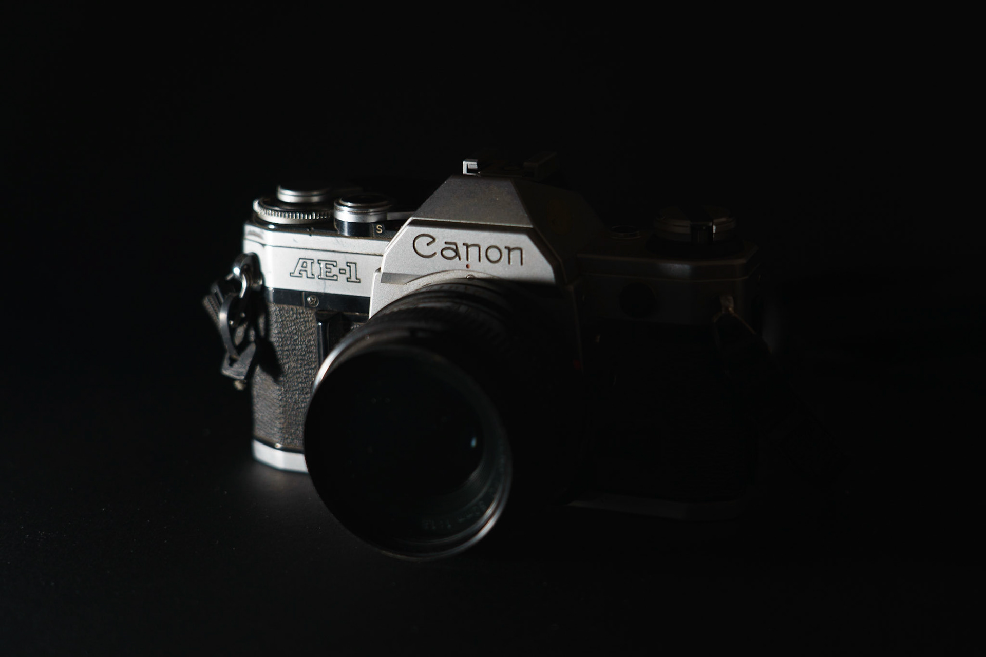Low Key Image: Canon camera on black paper, 20201107, MILLER, Utilizing the black backdrop I was able to get this low key image affect and utilize side lighting to emphasized the interesting lines of the camera without having a completely lit subject. Camera Settings: Sony A7II, ISO 200, 65mm, f4.5, 1/10s