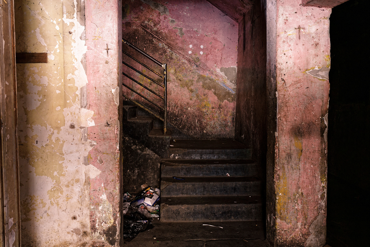 Stairway To The Cathouse 2014-2016 Photographic Print Fine Art Cotton Rag A0. The entrance of a dark building now opperating as a brothel stands pink with crosses scratched into the walls on either side of the staircase. Ladies charge R25 per customer of which R5 goes to the 'Landlord' who owns the room in the building they work from. The 'owner' bought the room for R400 from a building Hijacker.
