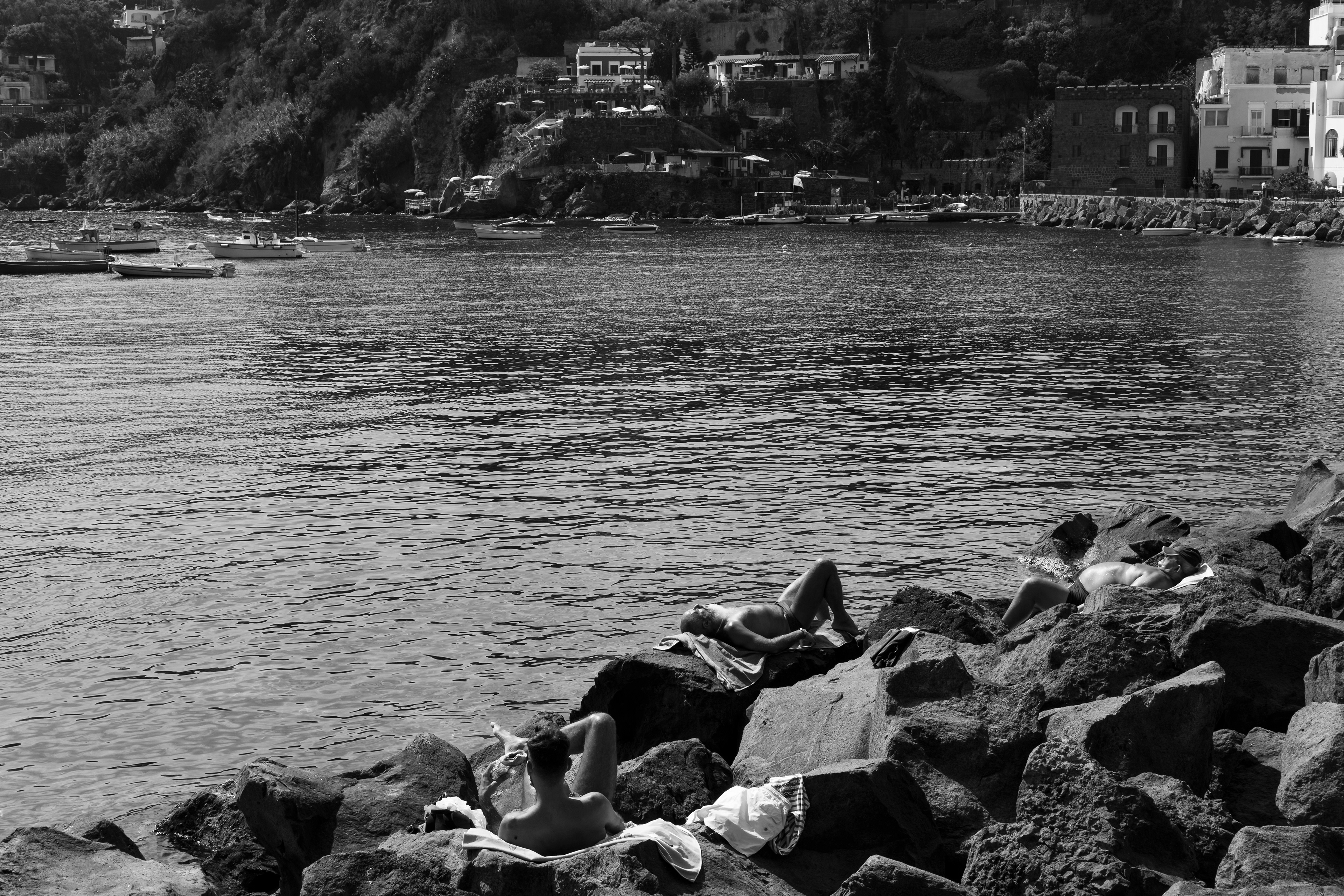 People resting on the rocks near the beach in Ischia, Italy