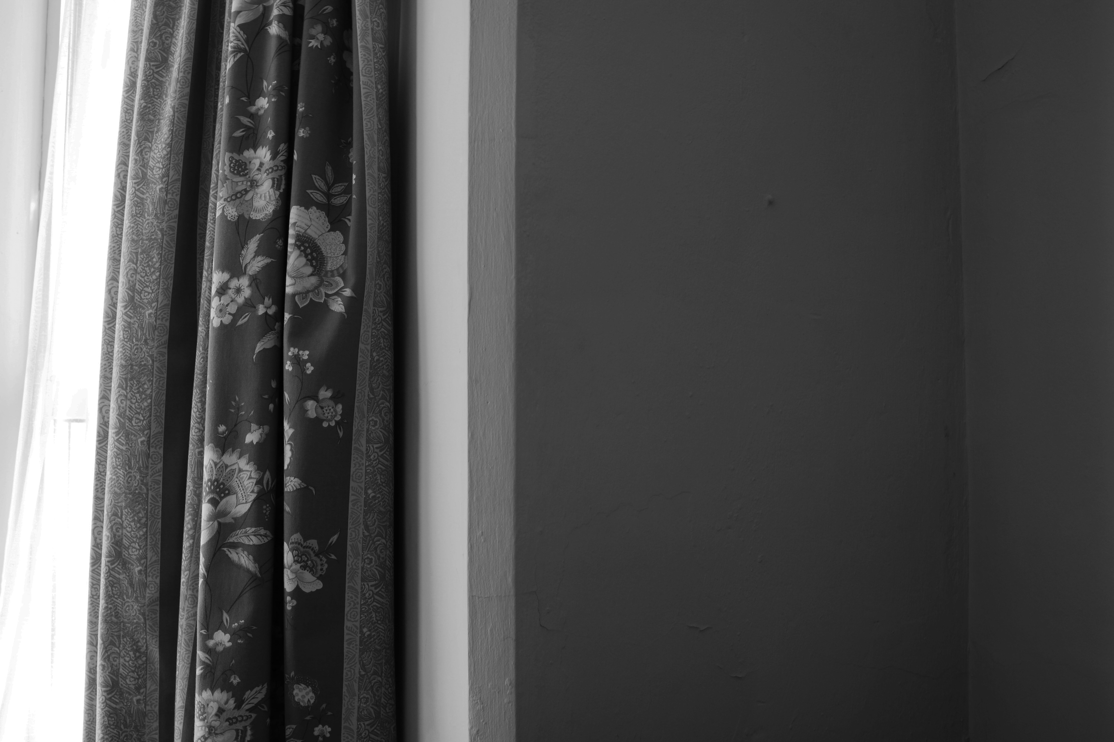 Dark corner of the room contrasting with the light in from the window, divided by a floral curtain