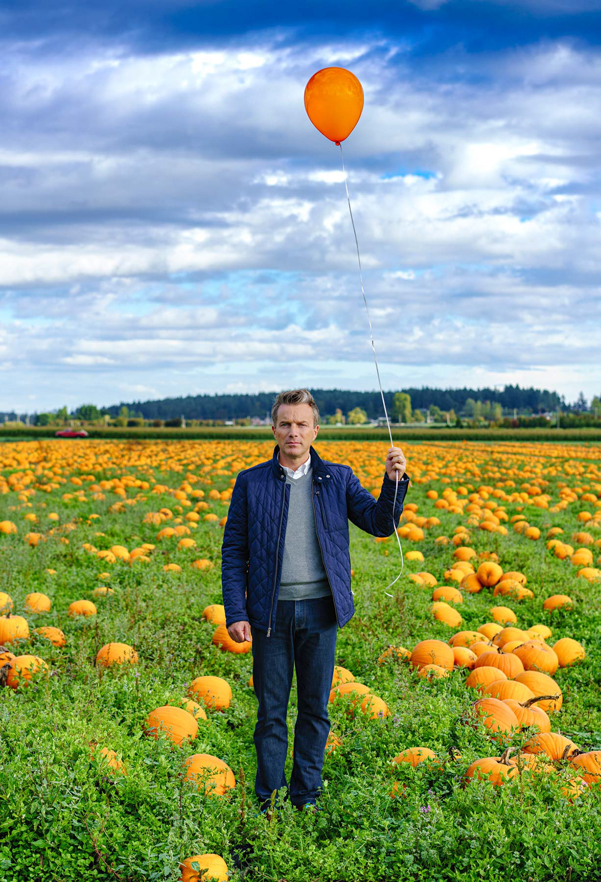 Lone figure standing in field of pumpkins, holding orange balloon