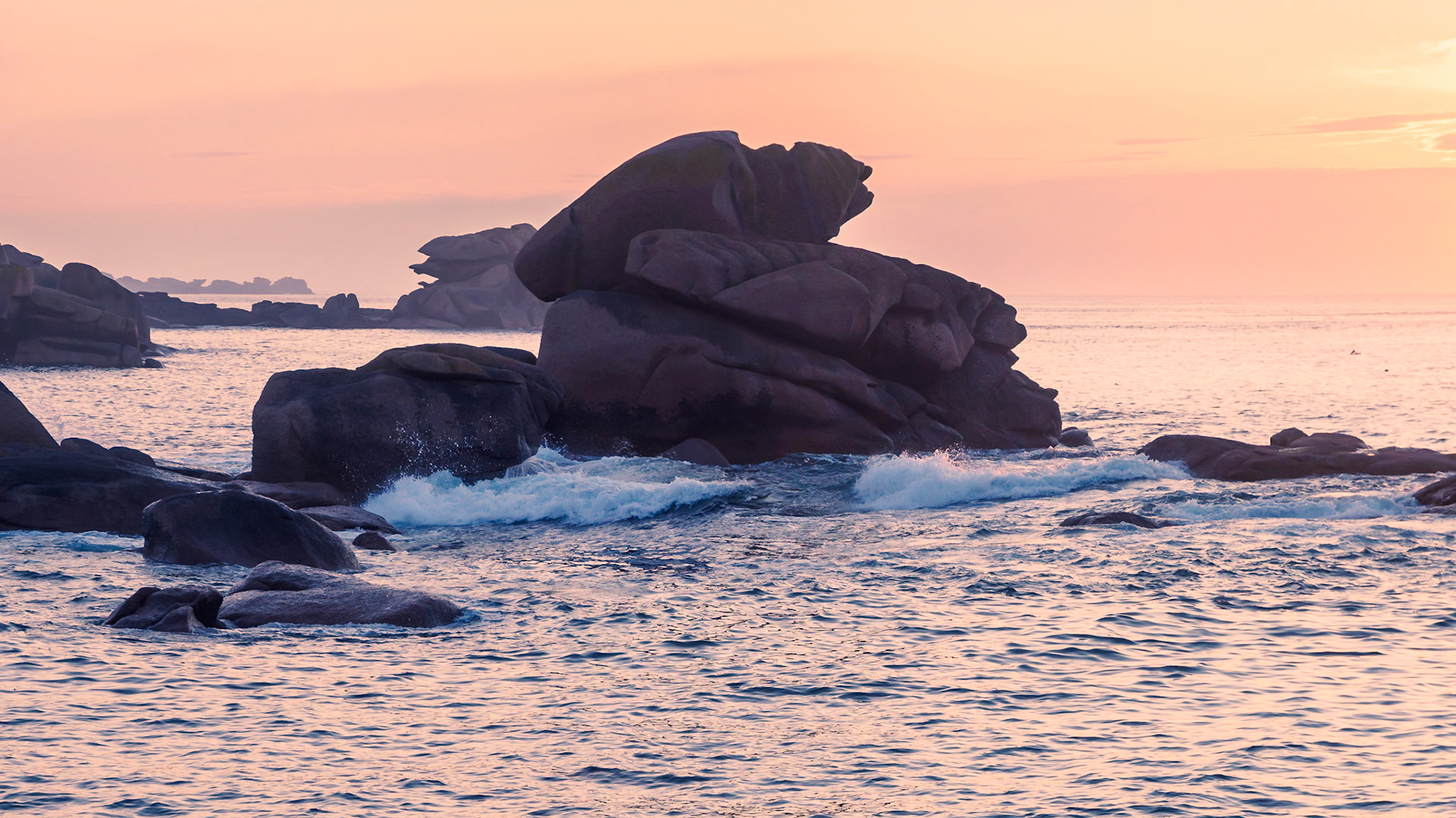 The slightly veiled sun setting over the English Channel at Ploumanach, France, reflecting in the water,  casting a soft dim light over the pink granite rocks. Can you see the pointing fingers ?