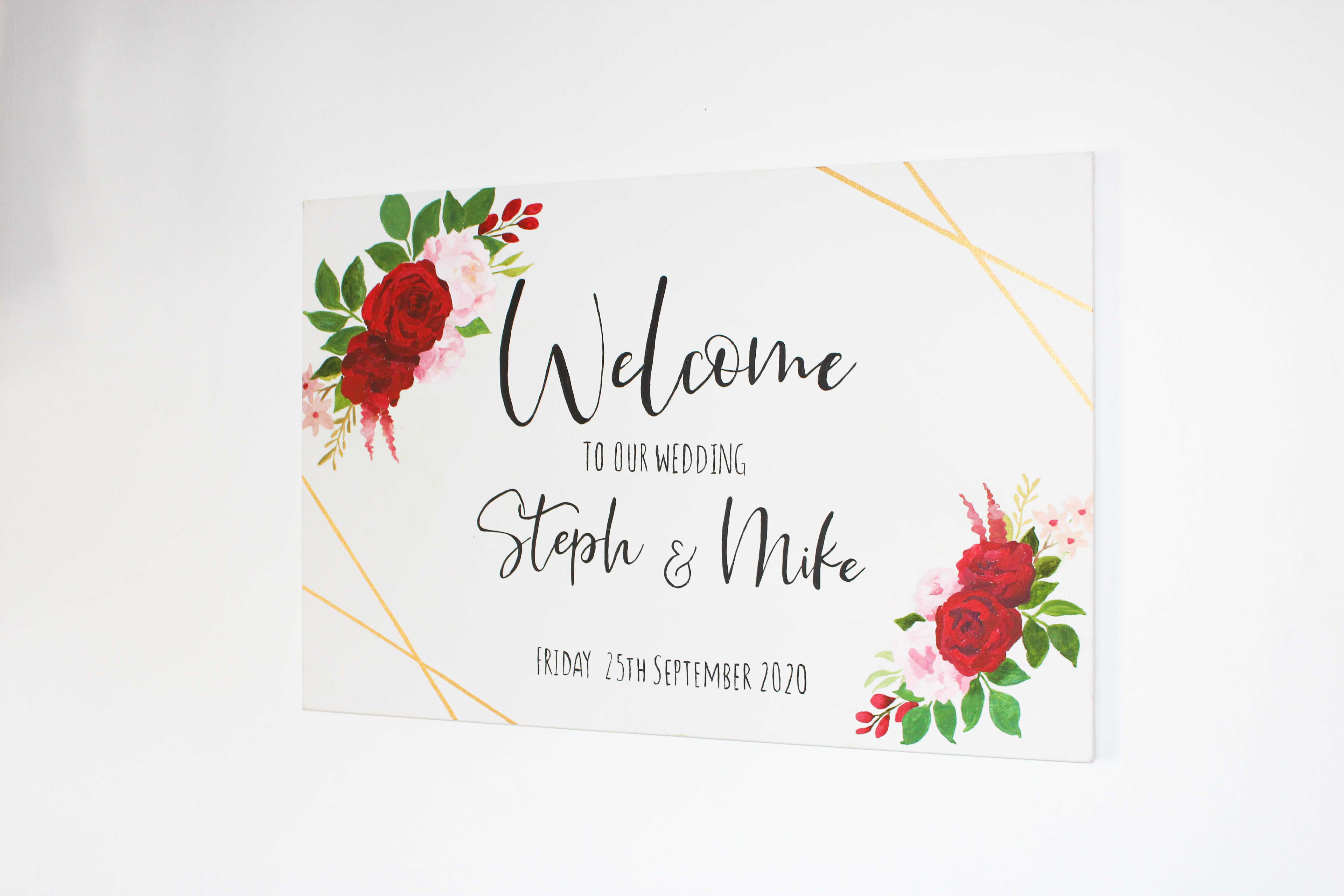 Unframed canvas with red, pink and green floral detail on top left and bottom right, gold geometric lines in opposite corners. Welcome to tech & Mike's Wedding & date in black