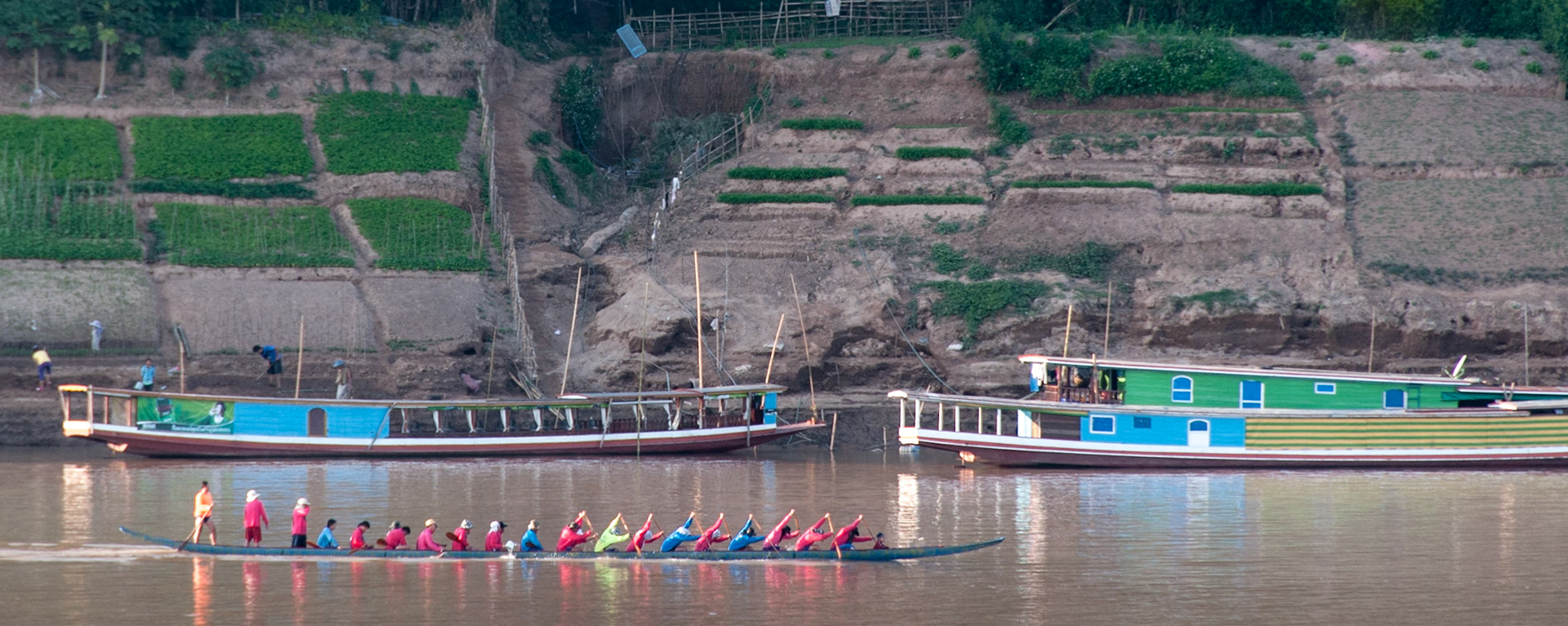 Laos, Luang Prabang, Mekong River, ferry boats and men paddling a dragon boat