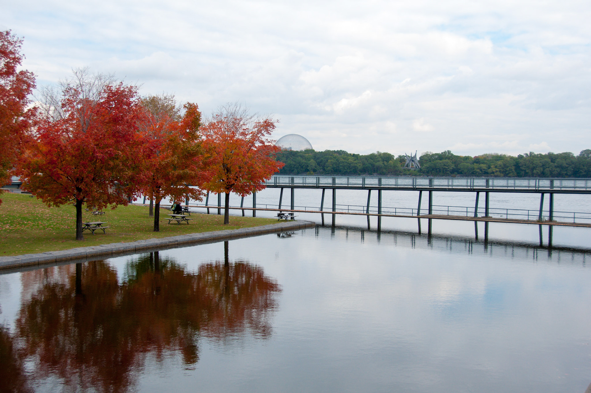 Green grass, grey skies and red leaves along the St Lawrence River in Montreal.  The Biosphere, built as the United States Pavillion for the Montreal Expo in 1964, is in the background.