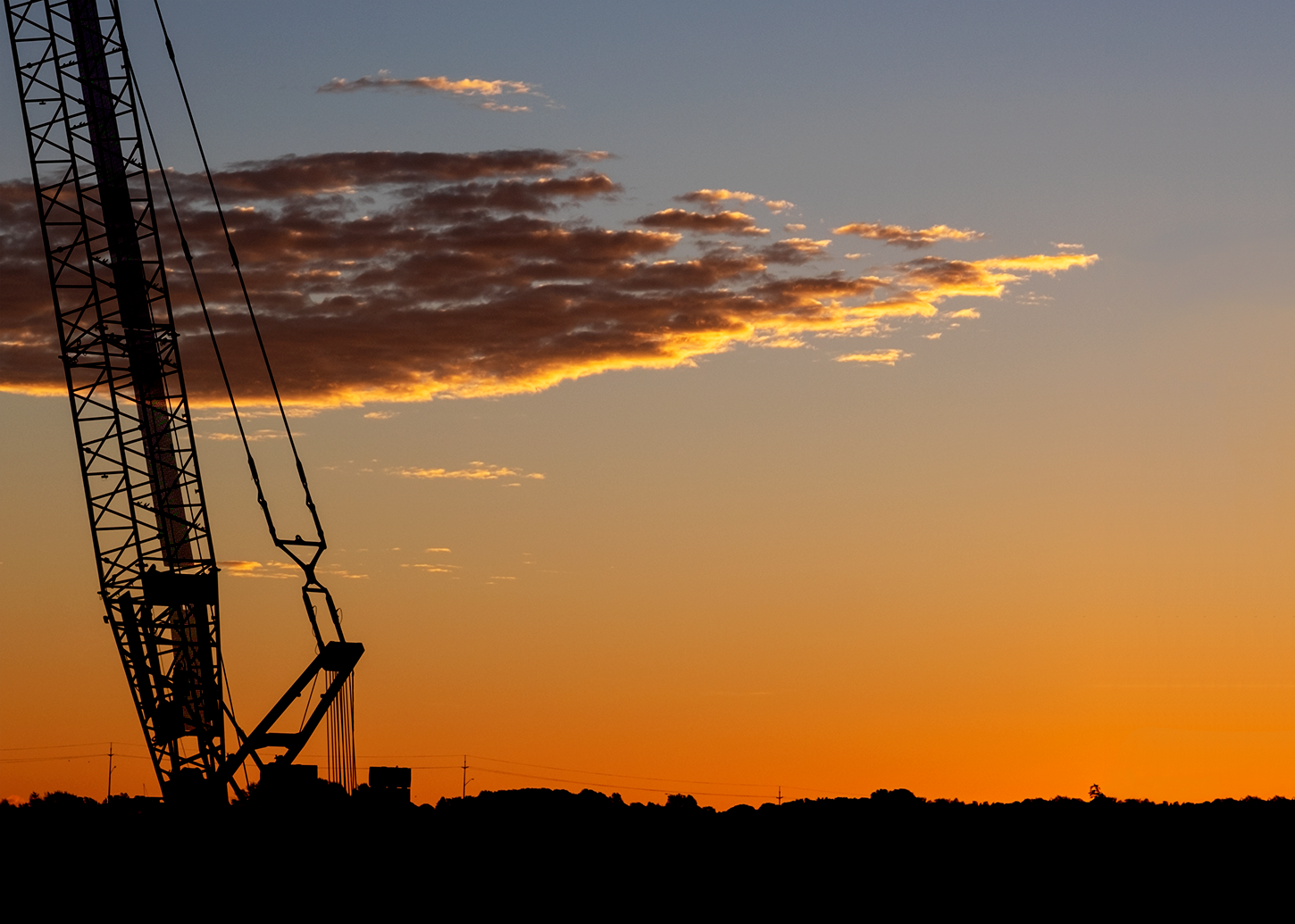The base of a crane appears in a deep orange sky; the metal rod hanging from the crane resemble a harp