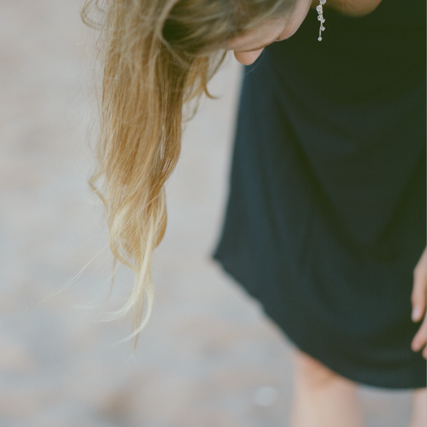 A single crystal earring dangles from a woman in a blue dress as she looks down